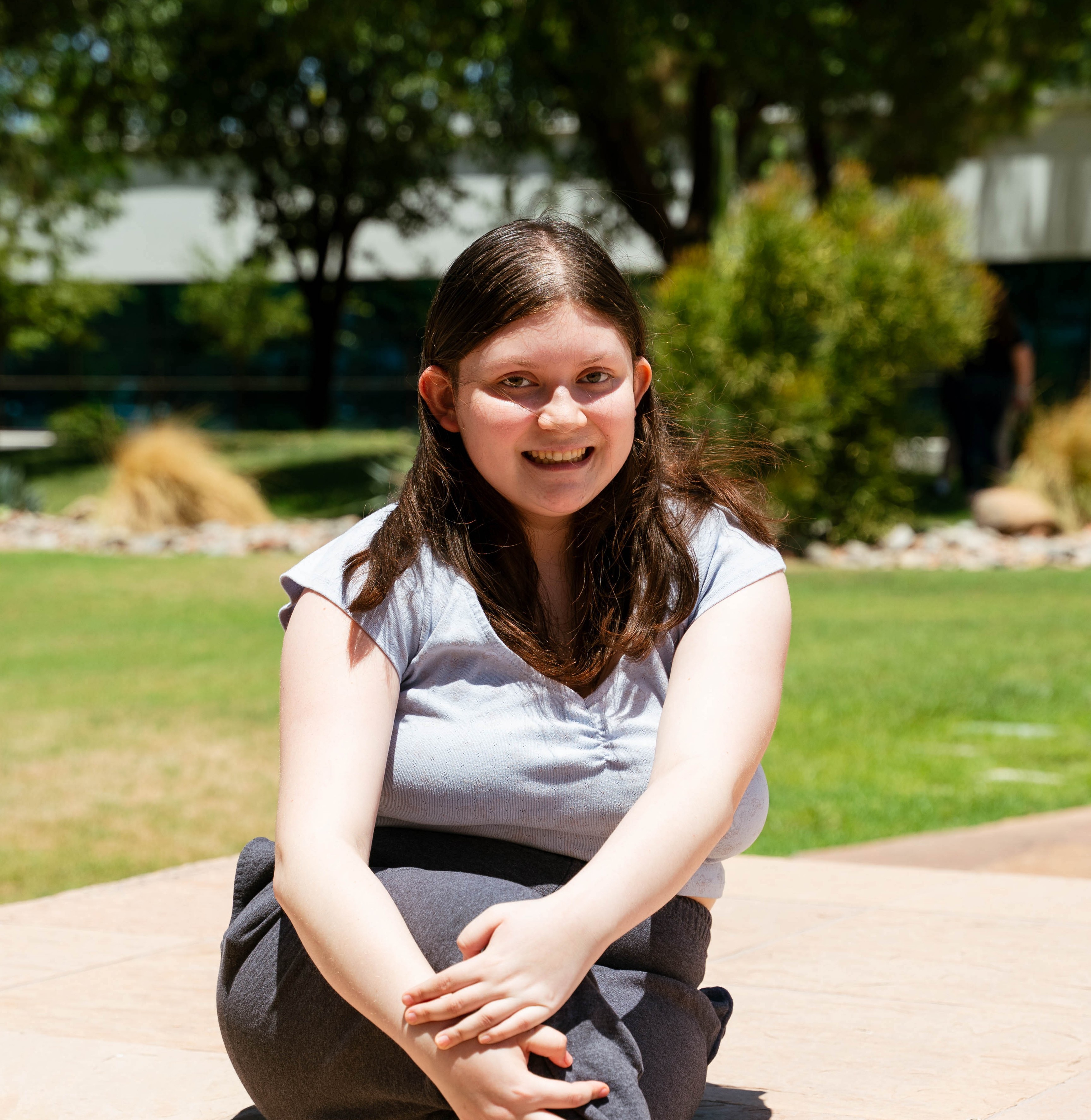 Valerie (2) sitting on wall with grass and bushes in background