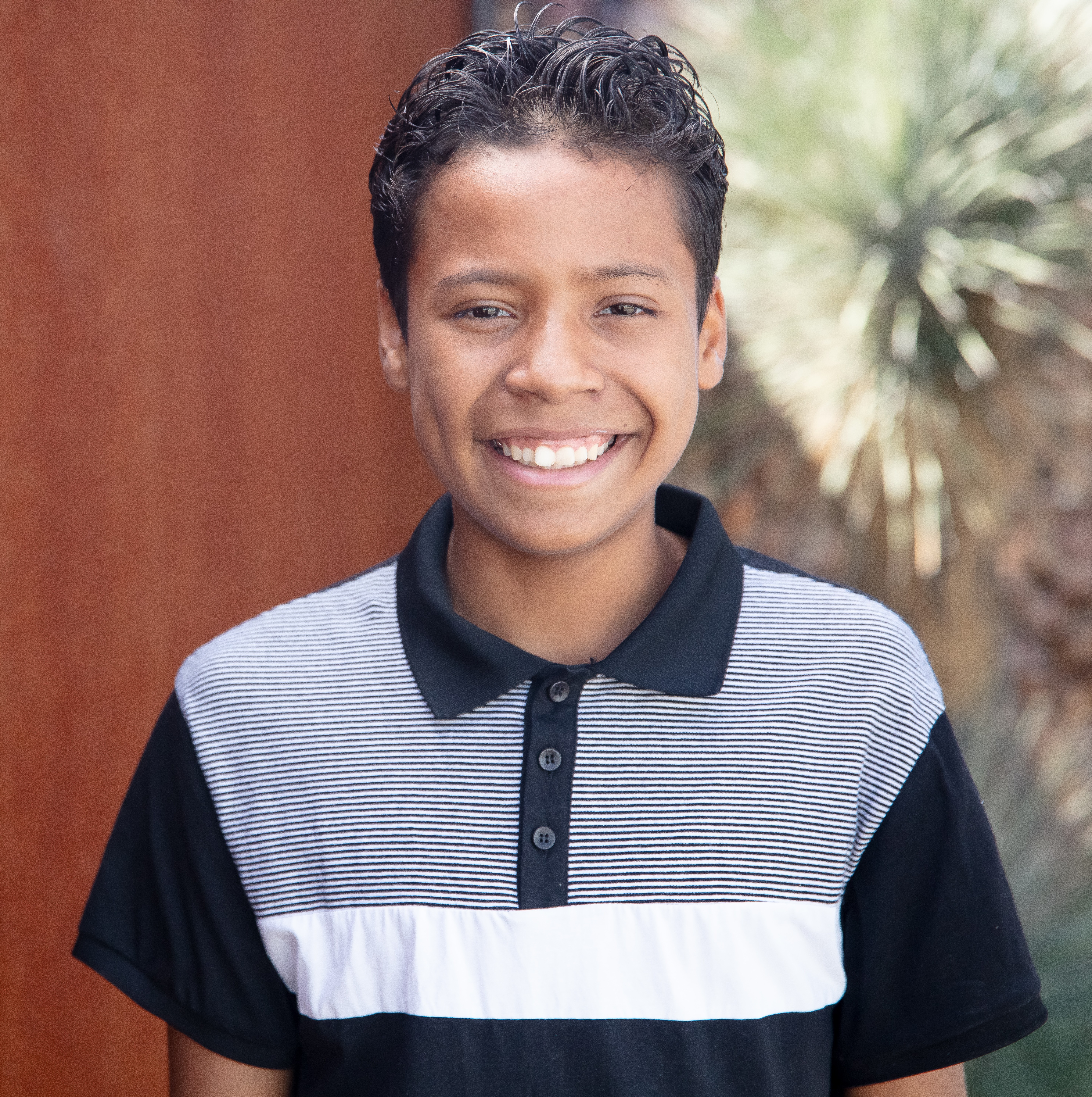 Skylar smiling with brown wall and palm in background